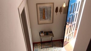 Un couloir avec des carreaux de sol à motifs, une petite table avec des livres, un tableau abstrait encadré et une porte bleue.