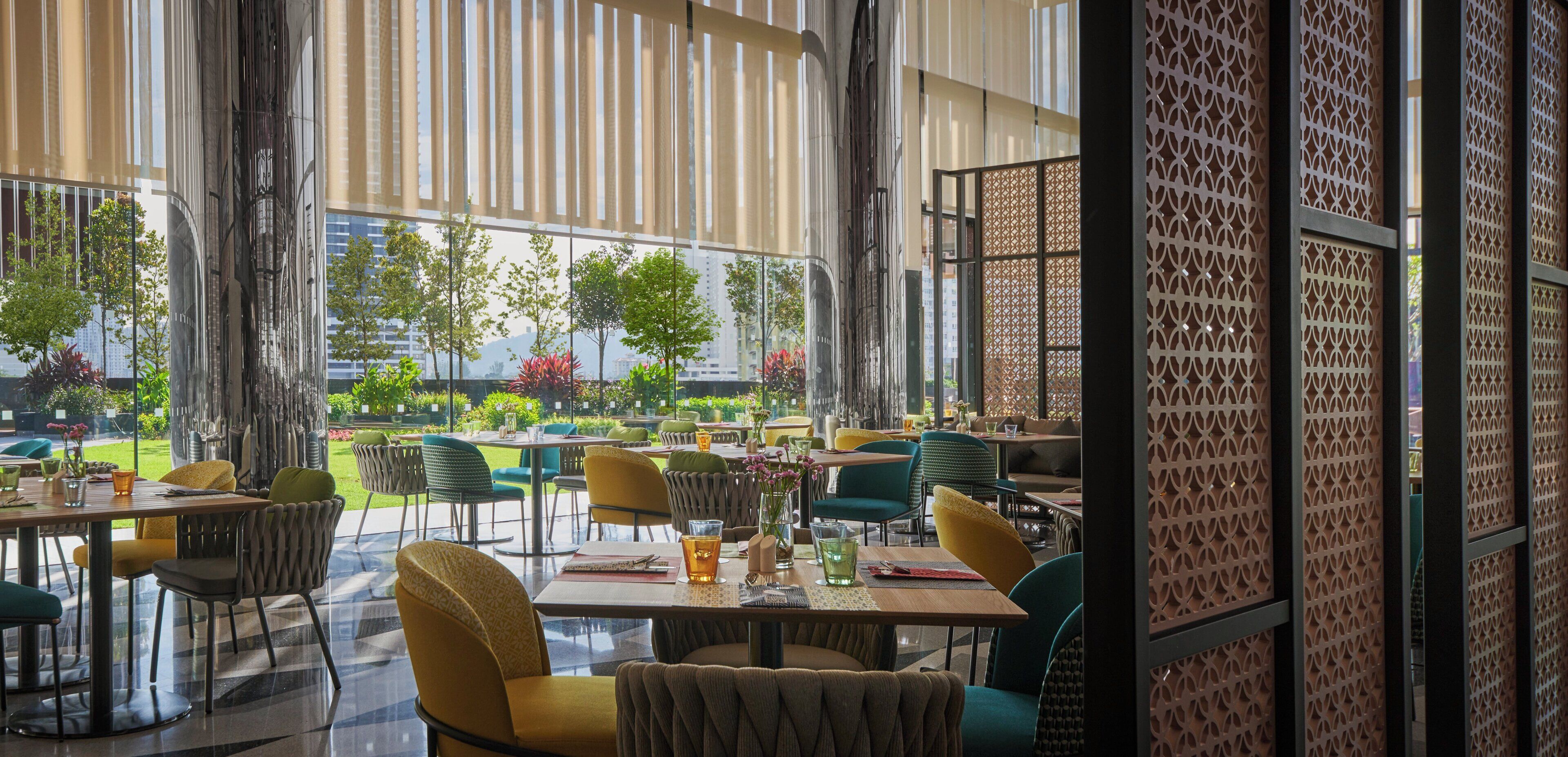 An indoor dining area with tables and chairs, large windows, and a view of greenery outside.