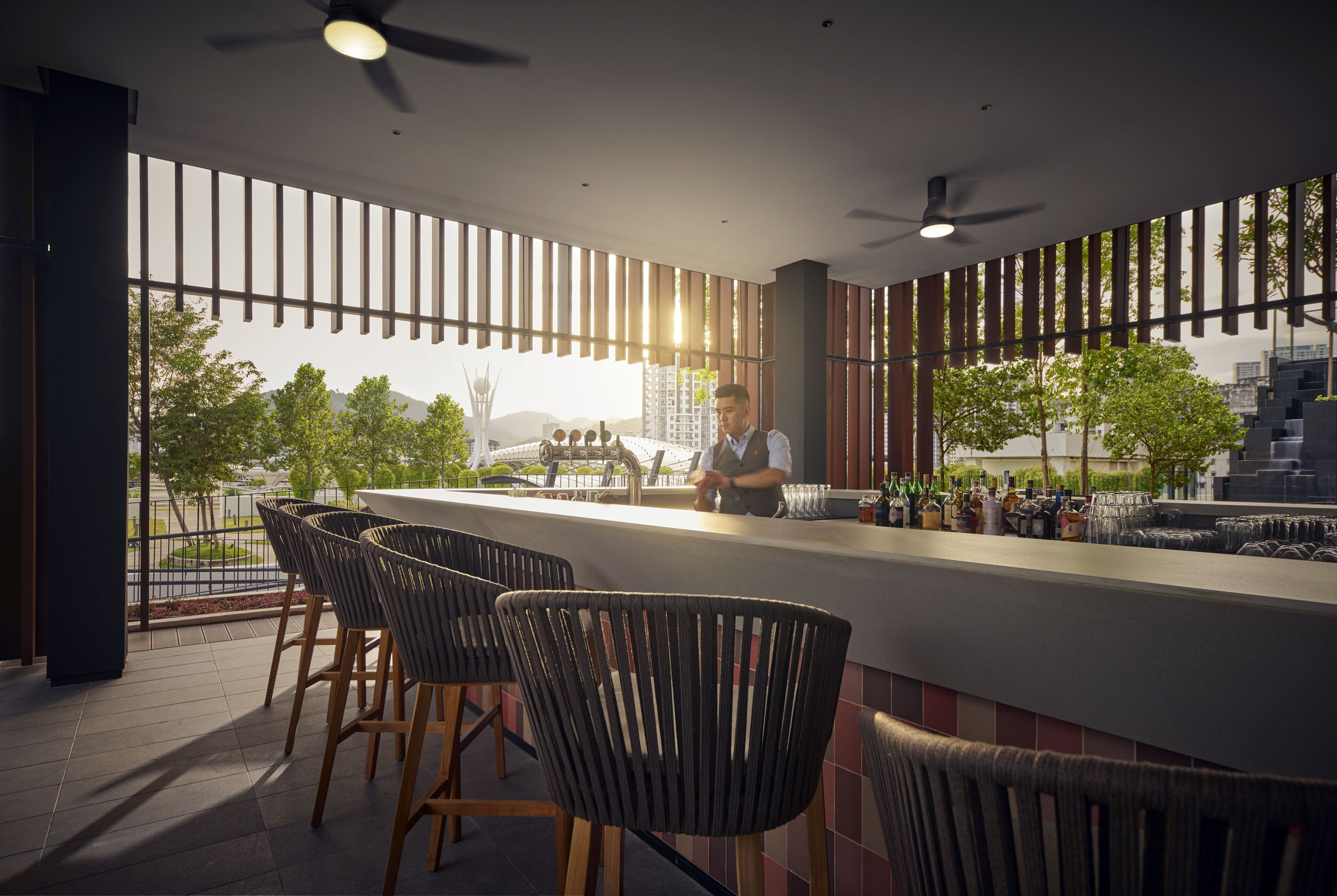A modern bar area with a bartender, bar stools, and a view of the cityscape.