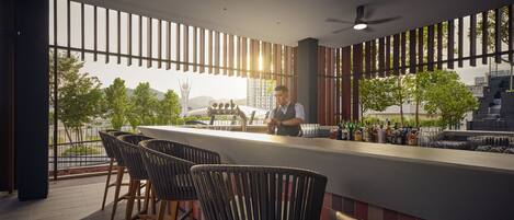 A modern bar area with a bartender, bar stools, and a view of the cityscape.