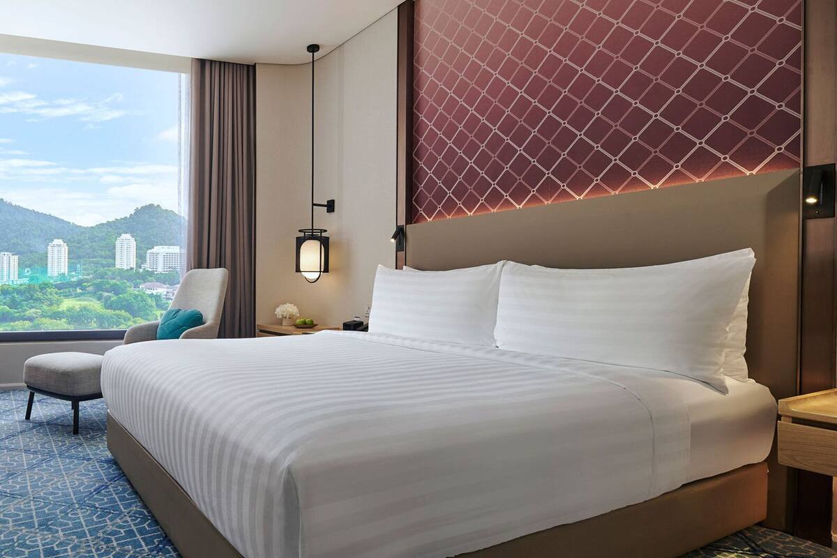 Hotellihuone, jossa on suuri sänky, tuoli, yöpöytä ja näkymä rakennuksiin ja viheralueille.