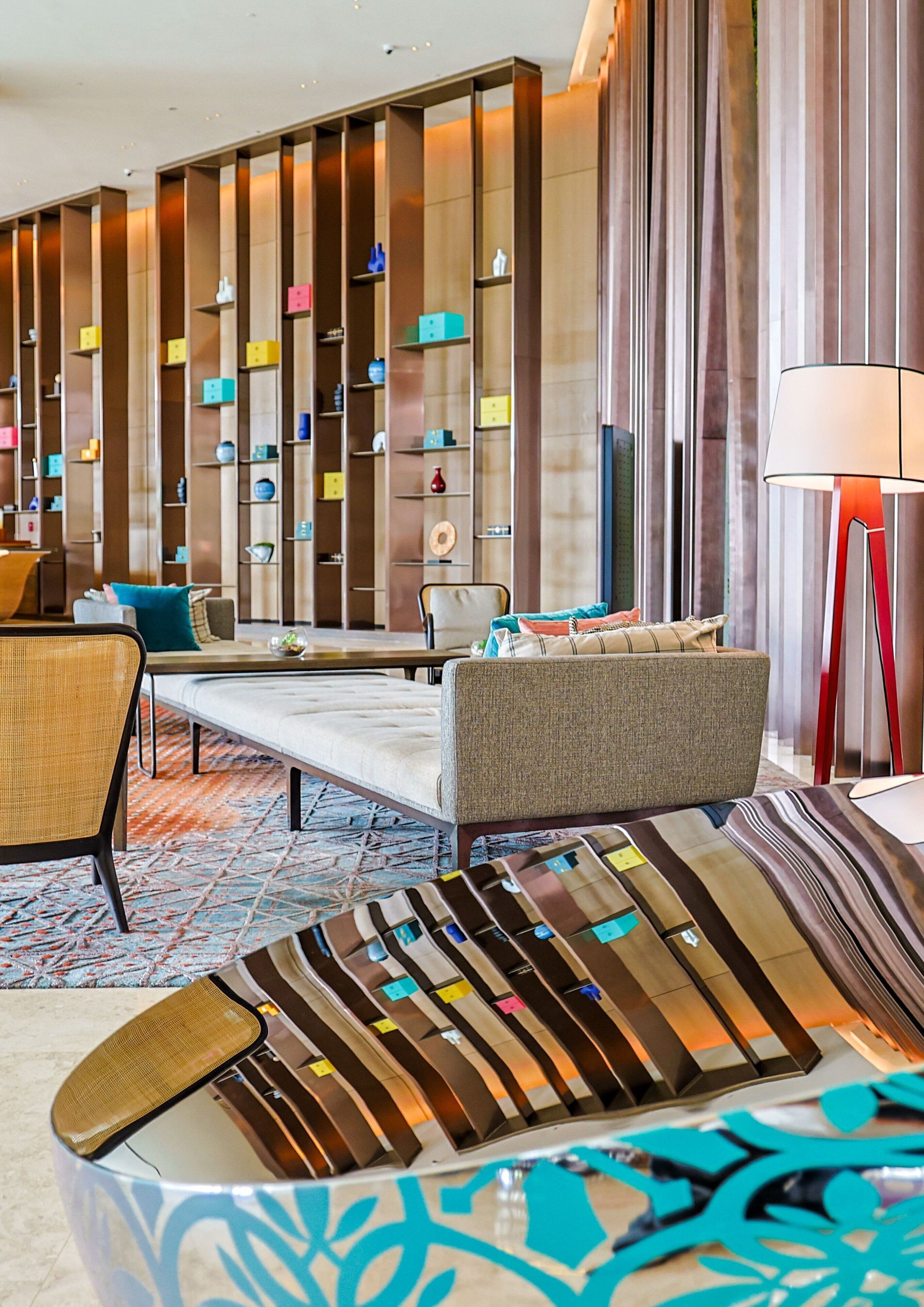 A modern hotel lobby with a sofa, chairs, a coffee table, a patterned rug, and a wall with colorful storage units.