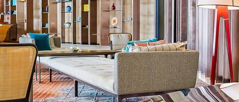 A modern hotel lobby with a sofa, chairs, a coffee table, a patterned rug, and a wall with colorful storage units.