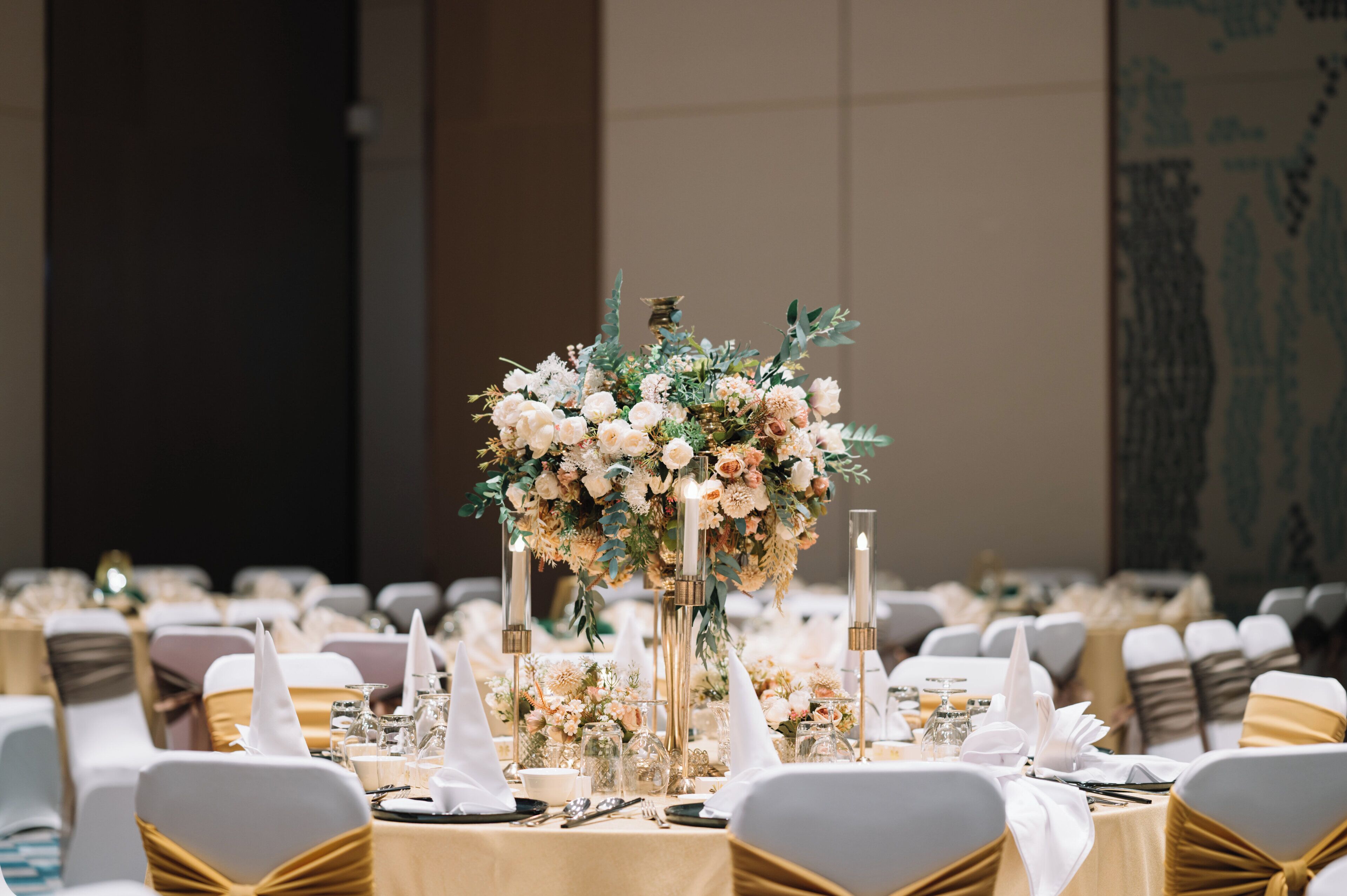 Une salle de banquet avec des tables rondes dressées pour un événement formel, agrémentées de compositions florales et recouvertes de nappes blanches.