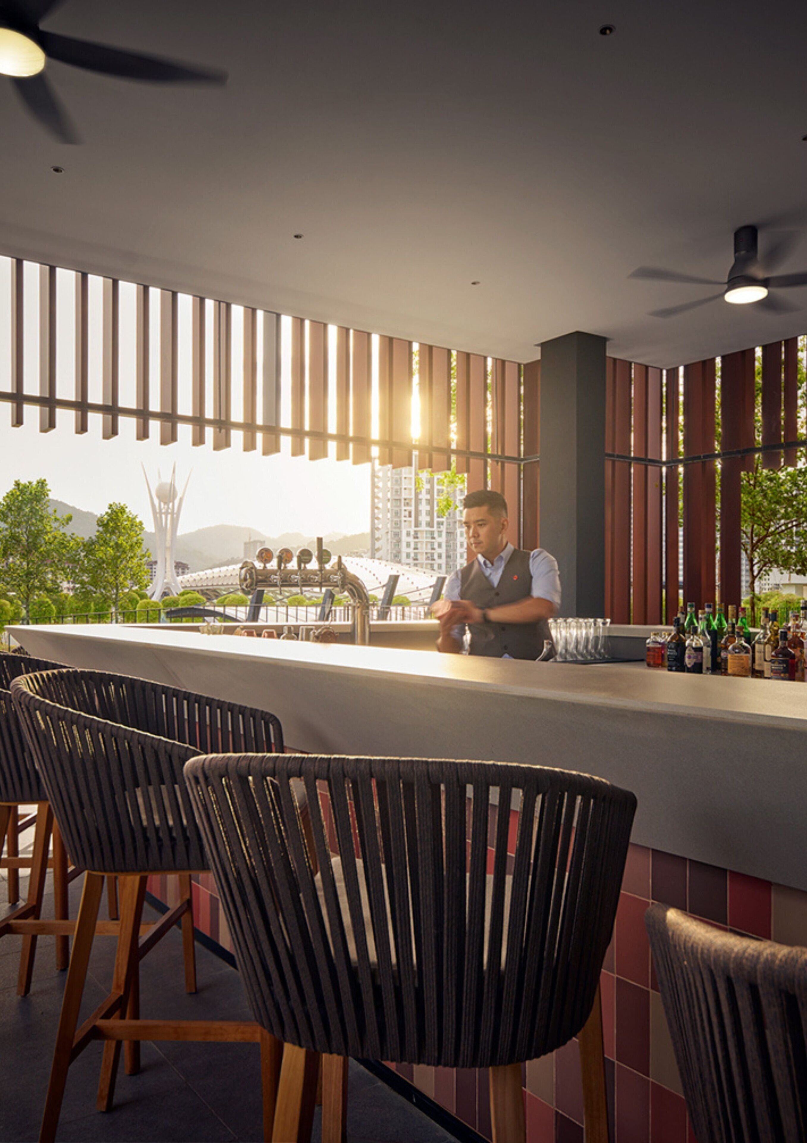 A bar area with a bartender, high chairs, and a view of a cityscape.