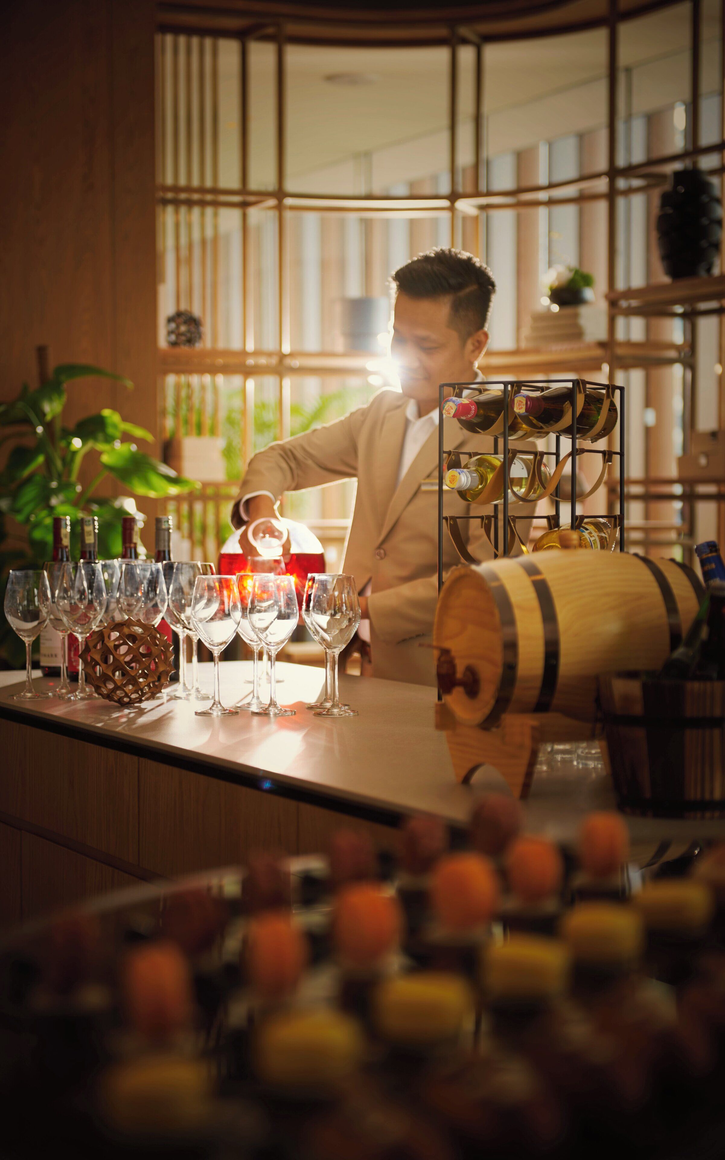 A bar area with a bartender, wine glasses, bottles, and a wooden barrel.