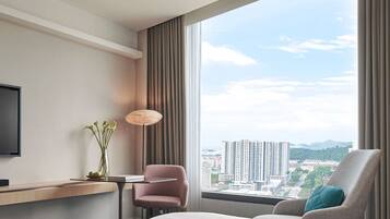 Et hotelværelse med stort vindue, seng, skrivebord, stol og fjernsyn.