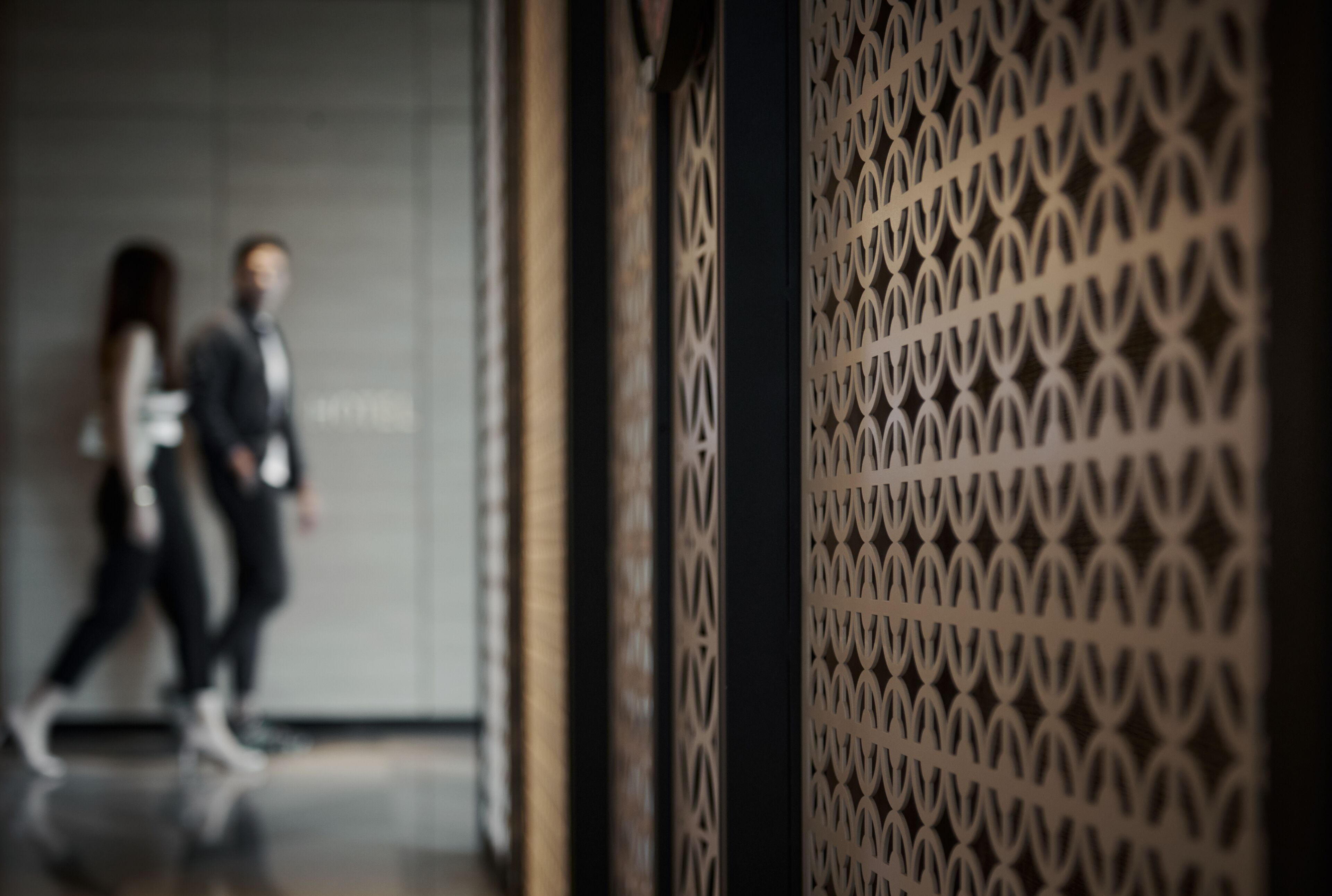 A corridor with a patterned wall and a door leading to a room.