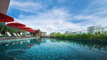 A swimming pool with tiled flooring, red umbrellas, and lounge chairs.