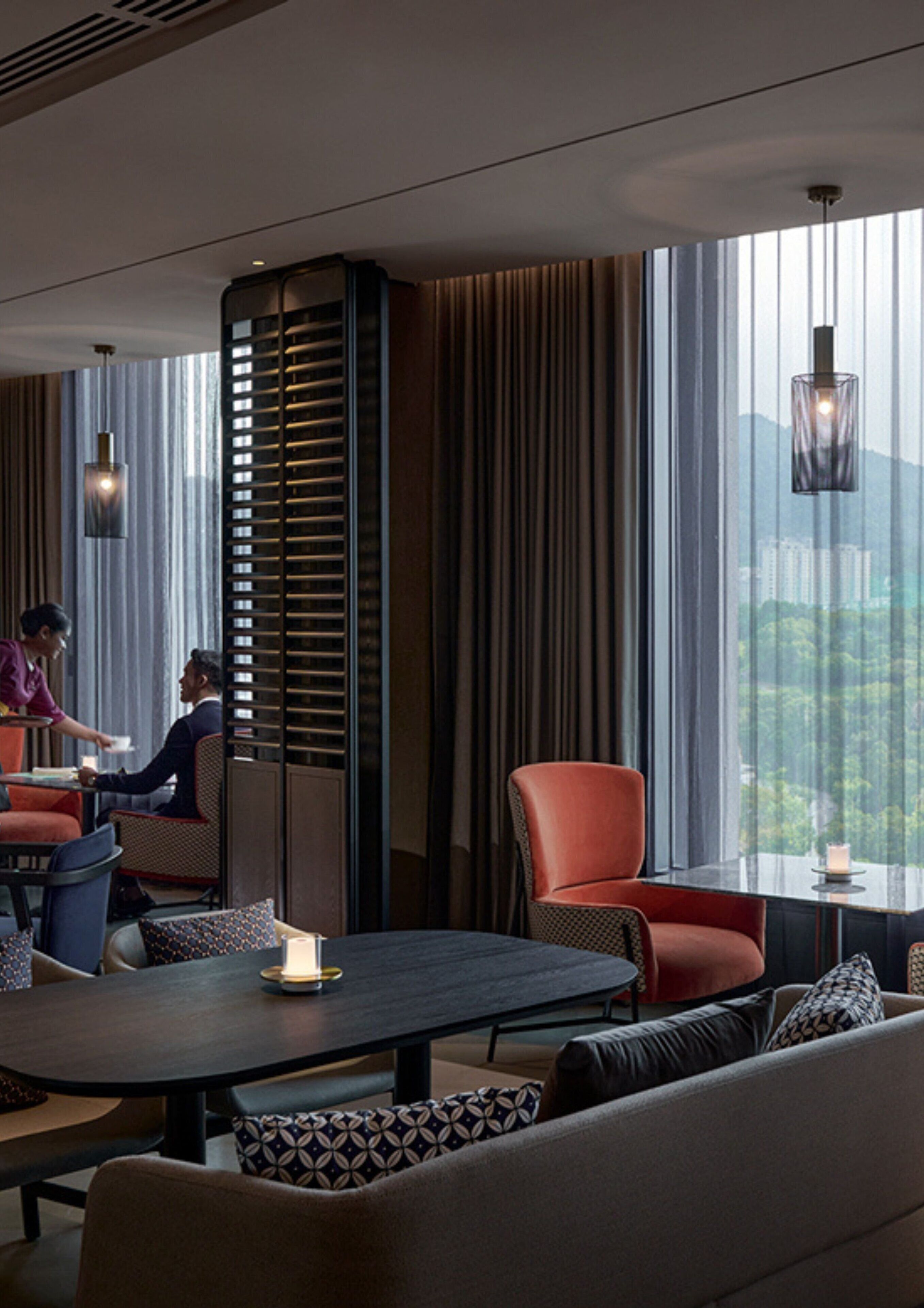Un hall d’hôtel moderne doté d’un espace repas, de grandes fenêtres et offrant une vue sur le paysage urbain.