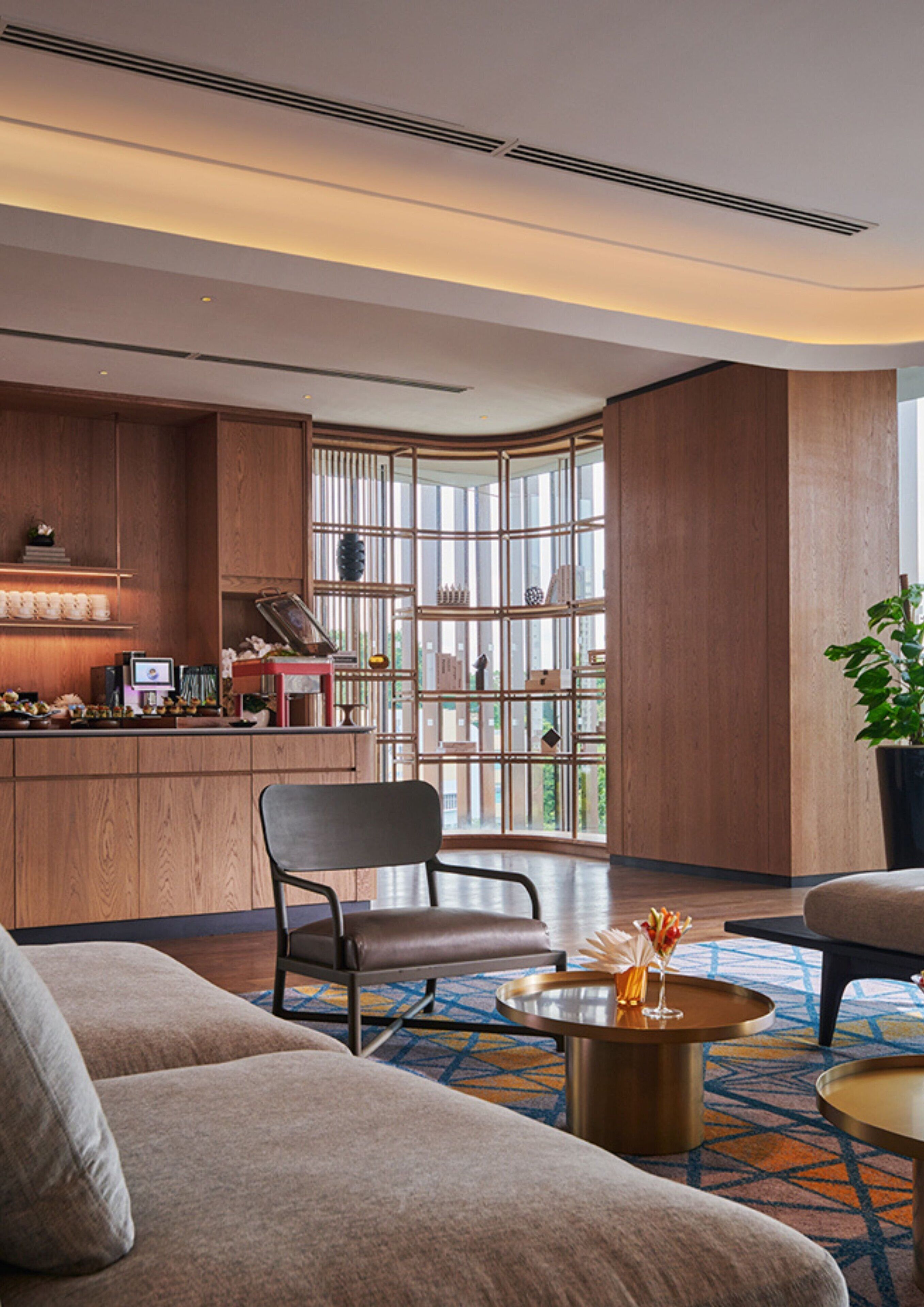 A modern hotel lobby with a wooden reception desk, seating area with sofas, and large windows offering a view of the city.