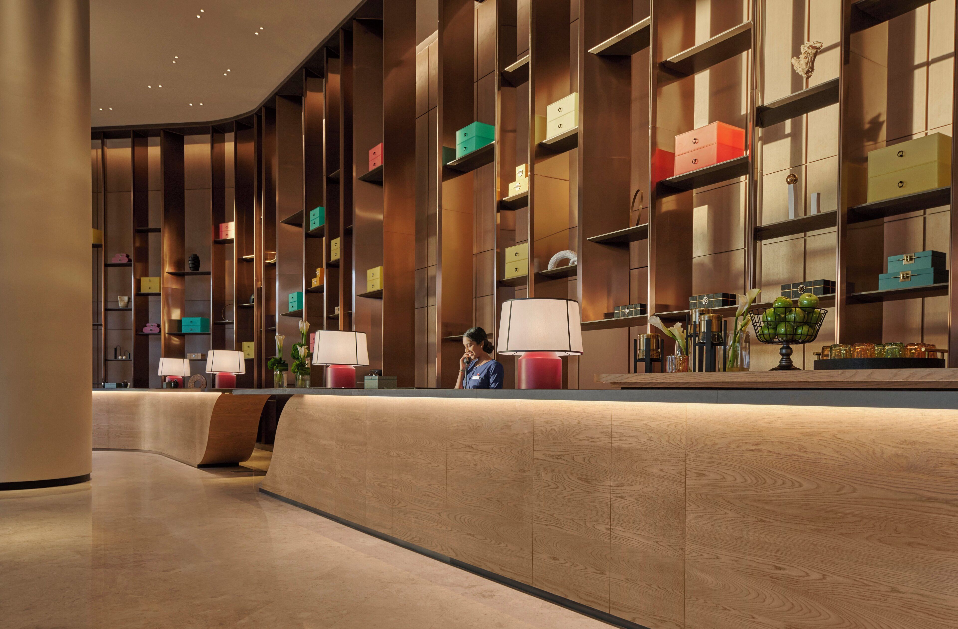 A modern hotel lobby with a curved reception desk, wooden paneling, and a variety of decorative items on shelves.