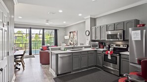 Une cuisine moderne avec des meubles gris, des appareils en acier inoxydable et une grande fenêtre donnant sur un balcon.