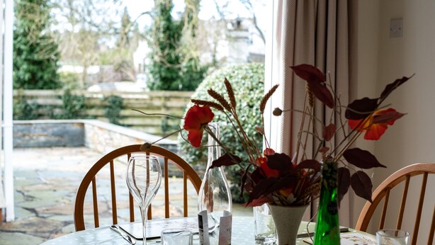 Ein Essbereich im Freien mit einem Tisch für zwei Personen, einer Blumenvase und Blick auf den Garten.