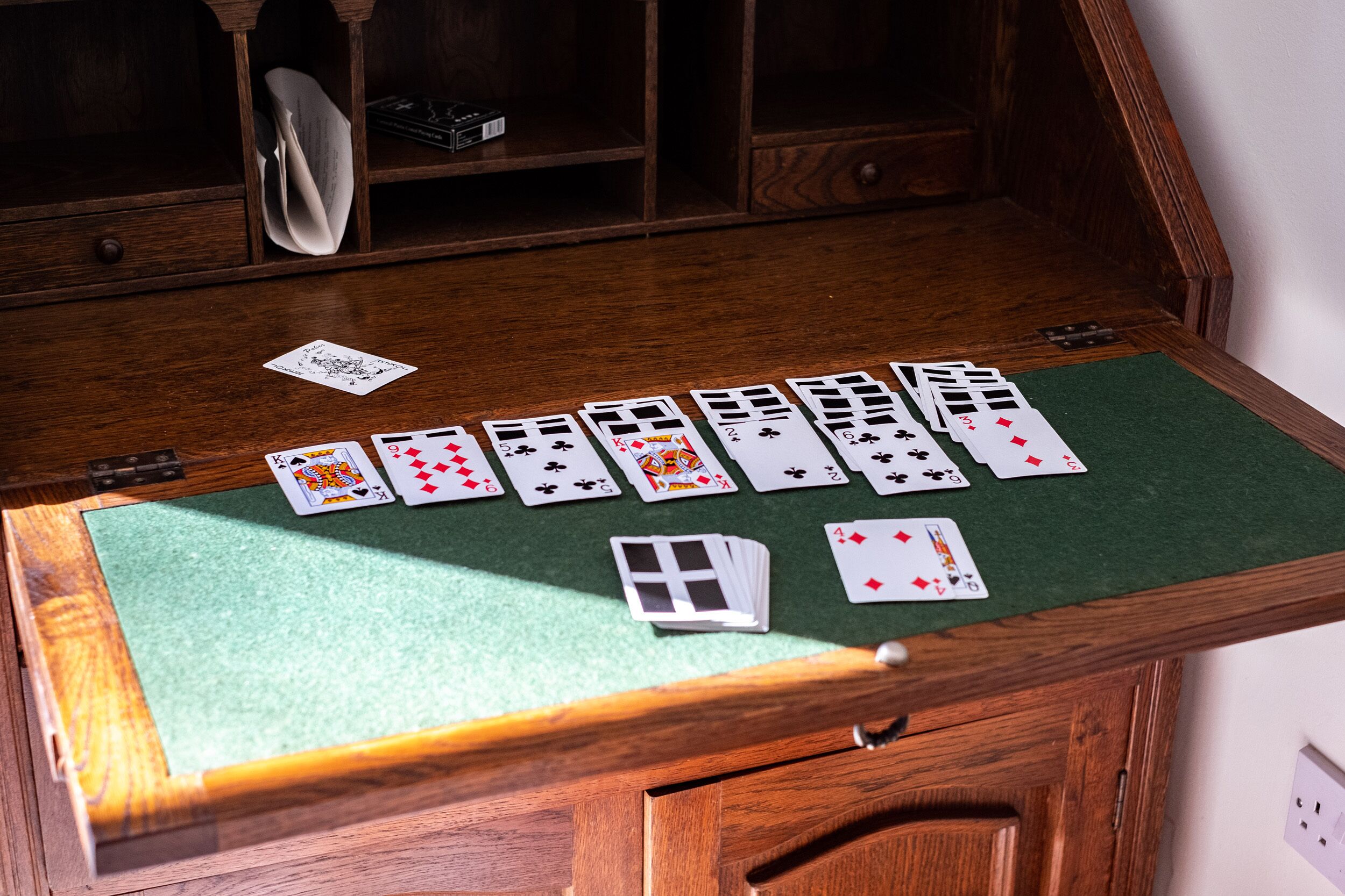 Une table en bois recouverte d’un tapis vert, sur laquelle sont disposés différents jeux de cartes.