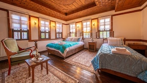 Habitación amplia con piso de madera, una cama grande, una cama más pequeña, una silla y una mesa con un objeto decorativo.