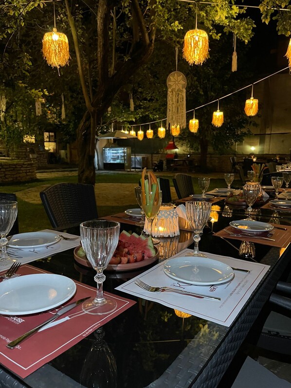 An outdoor dining area with tables set for a meal, string lights overhead, and a stone wall in the background. - Suleyman Bey Konak (Safranbolu)