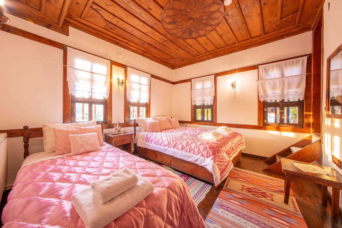 A cozy bedroom with two beds, wooden ceiling, and large windows with curtains.