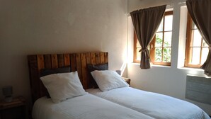 Una cama doble con sábanas blancas, un cabecero de madera, una mesita de noche con lámpara y una ventana con cortinas.