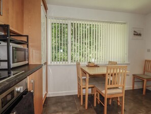 A kitchen with a dining table and chairs, a microwave, and a window with blinds. - 49 Atlantic Reach (Newquay)