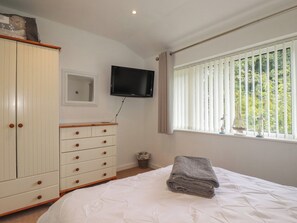 A bedroom with a bed, a television on the wall, a window with blinds, and a wardrobe. - 49 Atlantic Reach (Newquay)