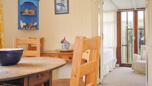 A dining area with wooden chairs and a round table, a blue cabinet with decorative items, and a framed picture on the wall. - Avoca (Wadebridge)