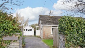 A stone wall with a sign reading "AVOCA," a gravel driveway leading to a house with a tiled roof, and a wooden gate. - Avoca (Wadebridge)