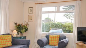 A cozy living room with a sofa, armchair, and a table with a bowl. A TV is on a stand to the right. - Avoca (Wadebridge)