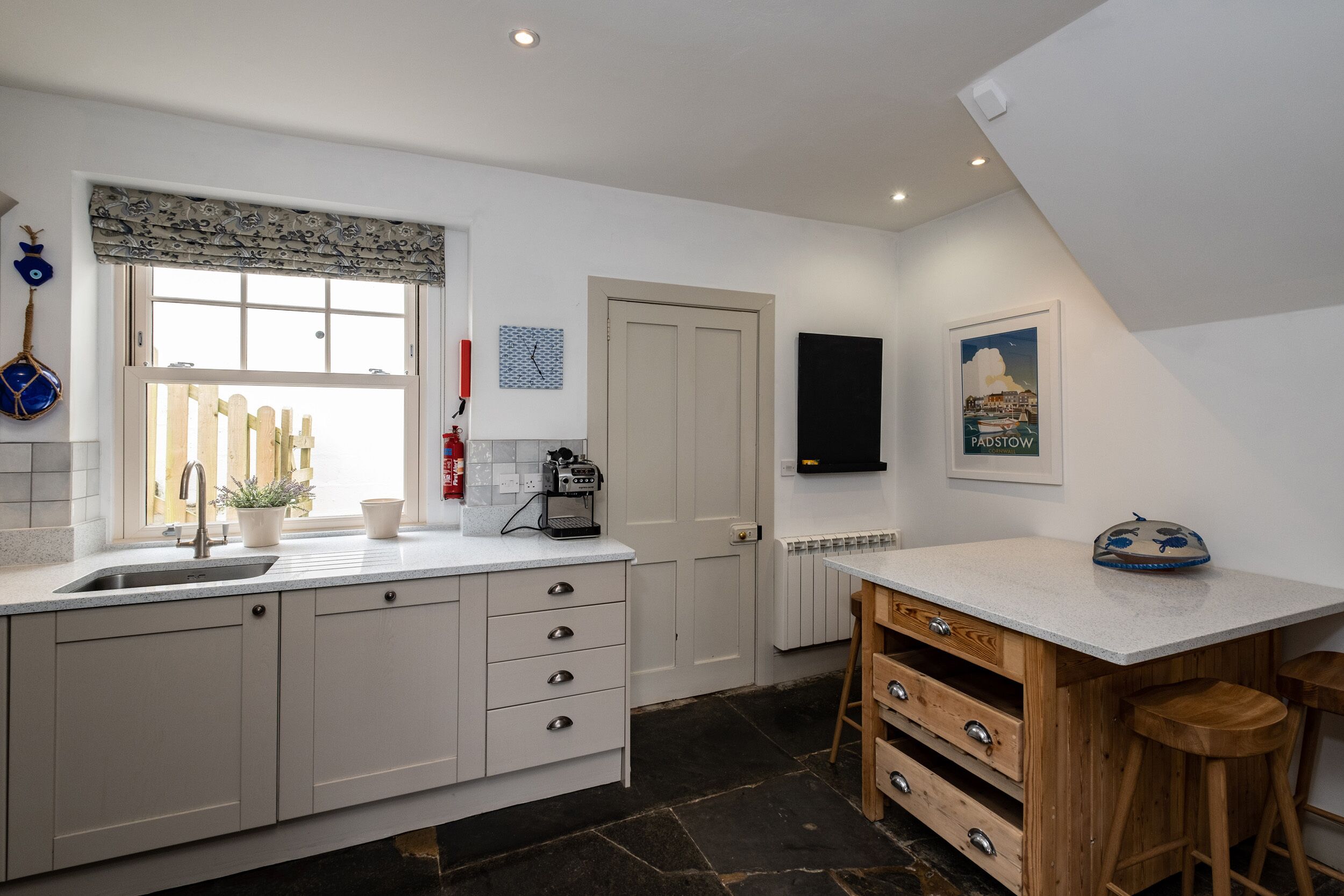 A modern kitchen with a large island, white cabinetry, a built-in oven, and a window with a patterned valance.