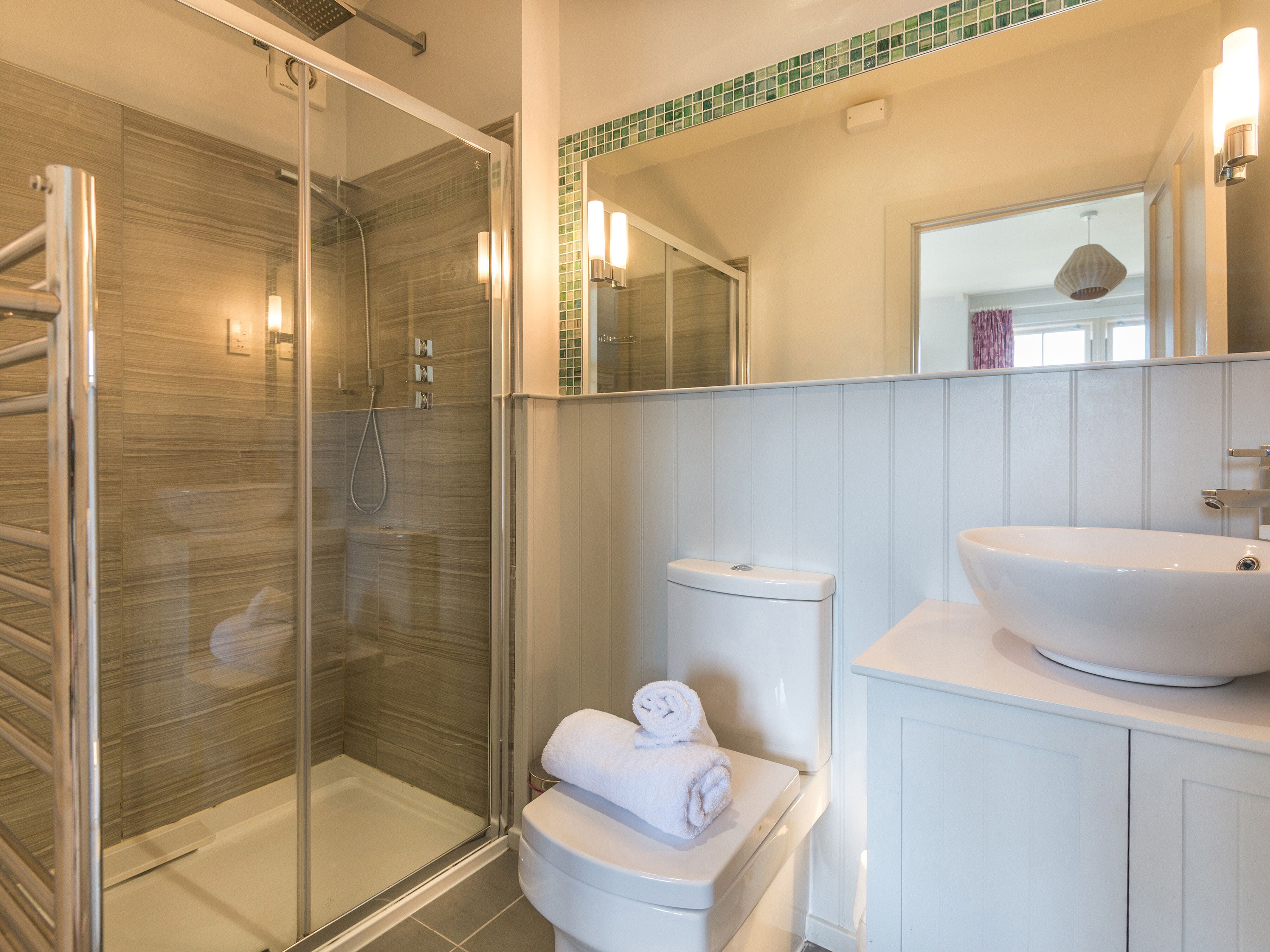 A modern bathroom with a glass-enclosed shower, a white toilet, and a large white sink.