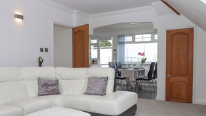 A modern living room with a white sectional sofa, a dining area with a table and chairs, and a view of the outdoors.