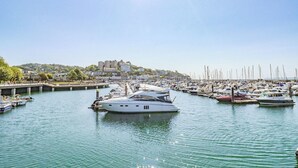 A marina with multiple boats docked, a bridge, and buildings in the background.