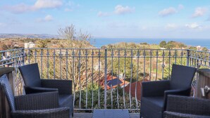 A balcony with wicker chairs and a view of the sea and landscape.