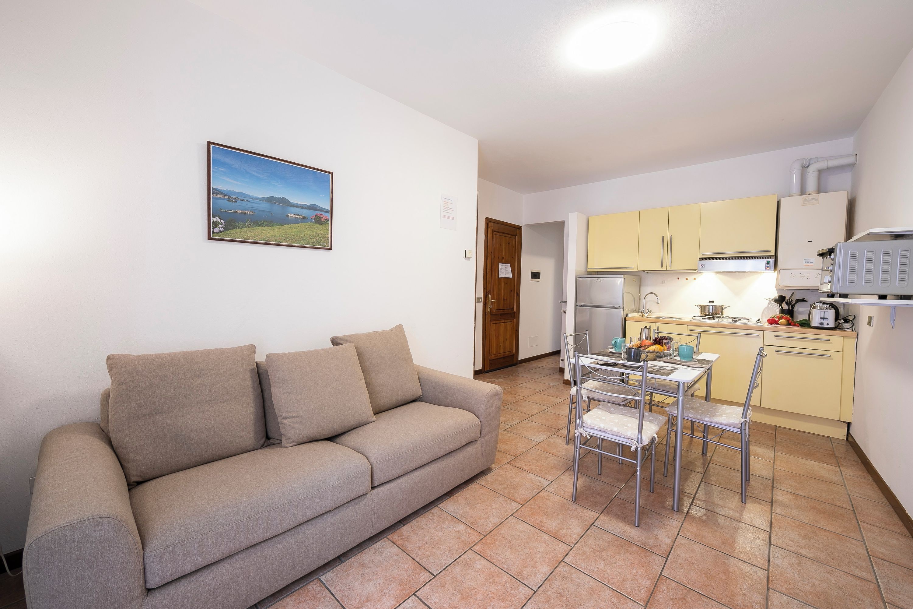 A living room with a sofa and a dining table with chairs. There is a kitchen area with cabinets and appliances.