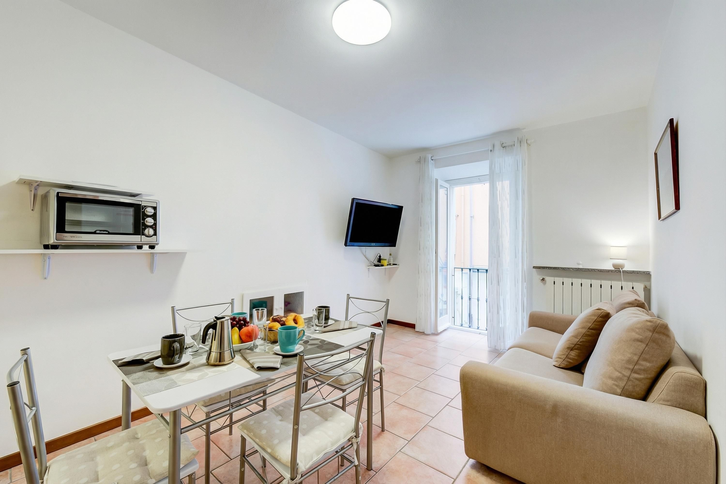 A compact living space with a kitchenette, a dining table, a sofa, and a TV mounted on the wall.