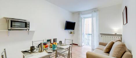A compact living space with a kitchenette, a dining table, a sofa, and a TV mounted on the wall.