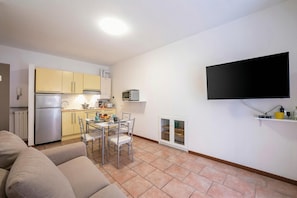 A compact living space with a kitchenette, a dining area, a flat-screen TV mounted on the wall, and a sofa. - Casa Dolce Casa Stresa 50m From Lake (Stresa)