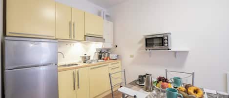 A compact kitchen with a refrigerator, microwave, and yellow cabinets. There is a dining table with chairs and a breakfast setting.