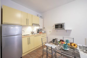 A compact kitchen with a refrigerator, microwave, and yellow cabinets. There is a dining table with chairs and a breakfast setting. - Casa Dolce Casa Central Stresa Apt 50m From Lake (Stresa)