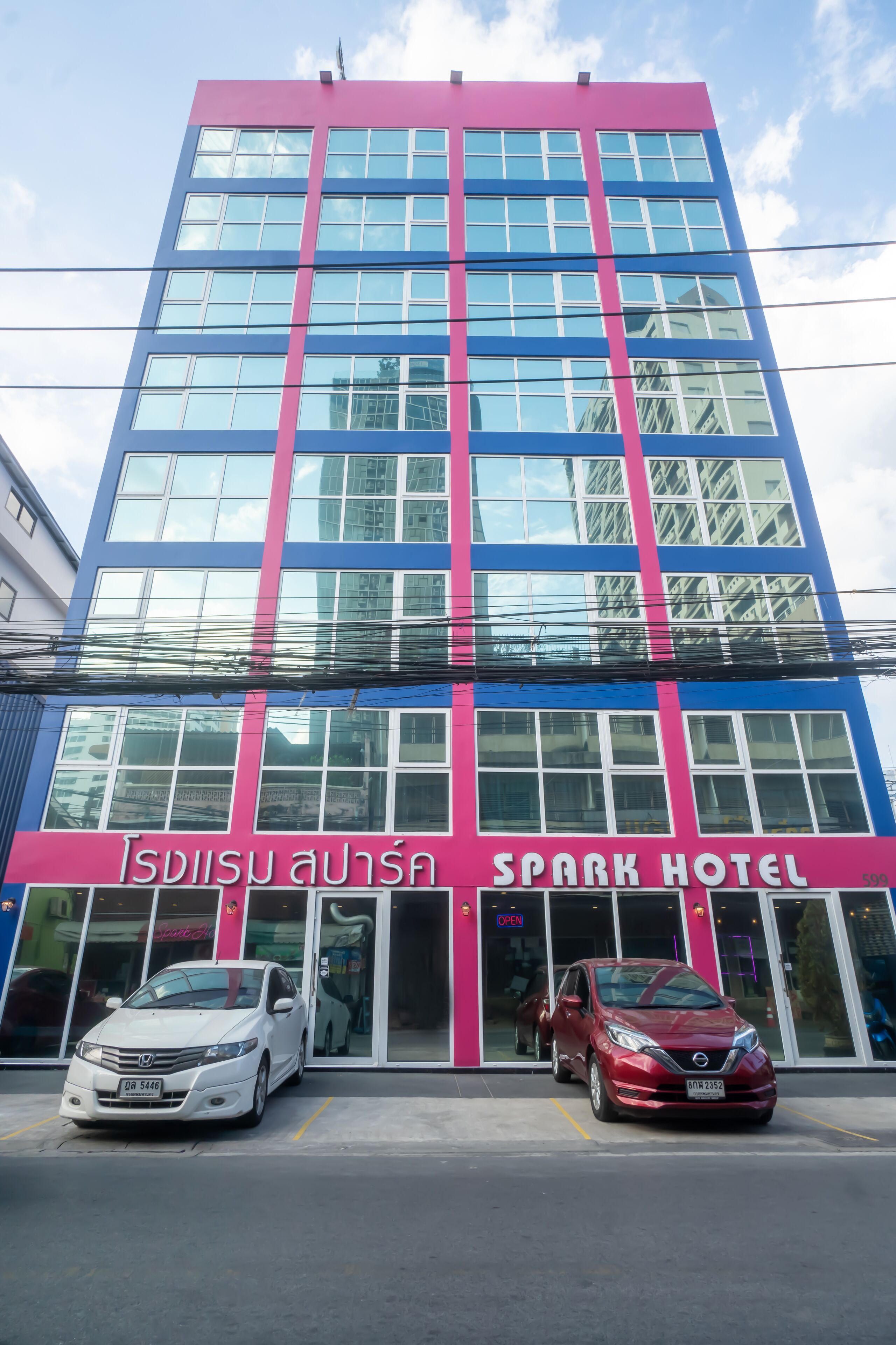 A multi-story hotel with a prominent pink and blue facade, large windows, and a visible car entrance. - Spark Hotel (Bangkok)