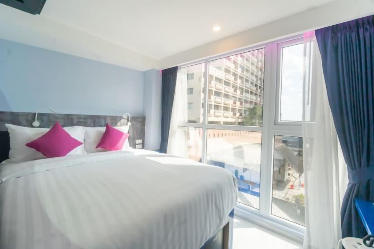 A hotel room with a large bed, a window with curtains, and a view of a building outside.