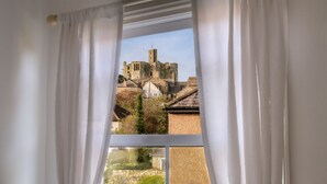 Quarto com grande janela que oferece vista para um edifício histórico de paredes de pedra e torre.