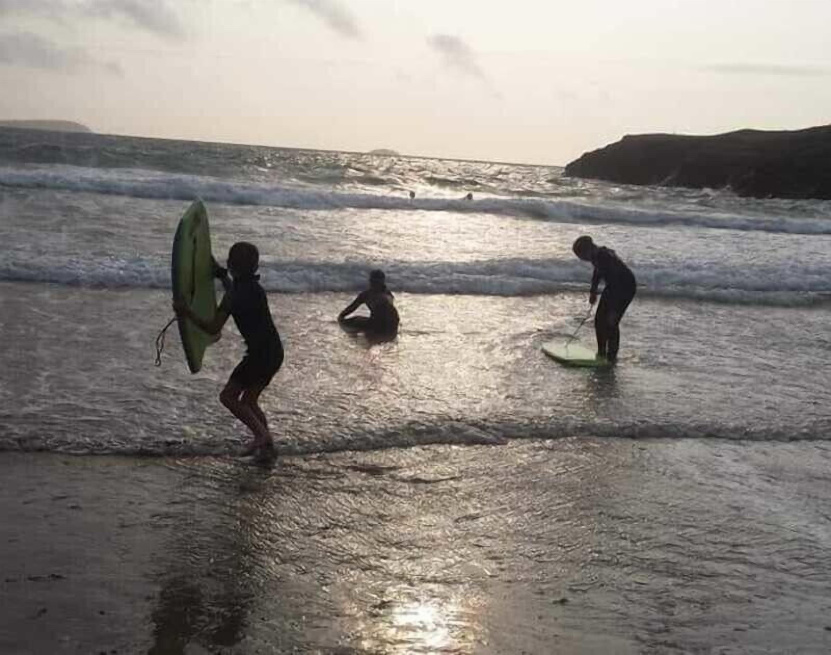 Una spiaggia con tre persone, una che porta un surfboard, un'altra seduta sulla sabbia e la terza in piedi con un surfboard.
