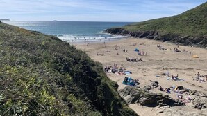 A beach with people sunbathing and swimming, surrounded by rocky cliffs and greenery.