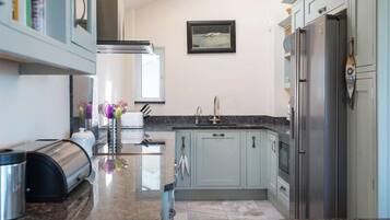 A modern kitchen with light blue cabinets, a stainless steel refrigerator, and a granite countertop.