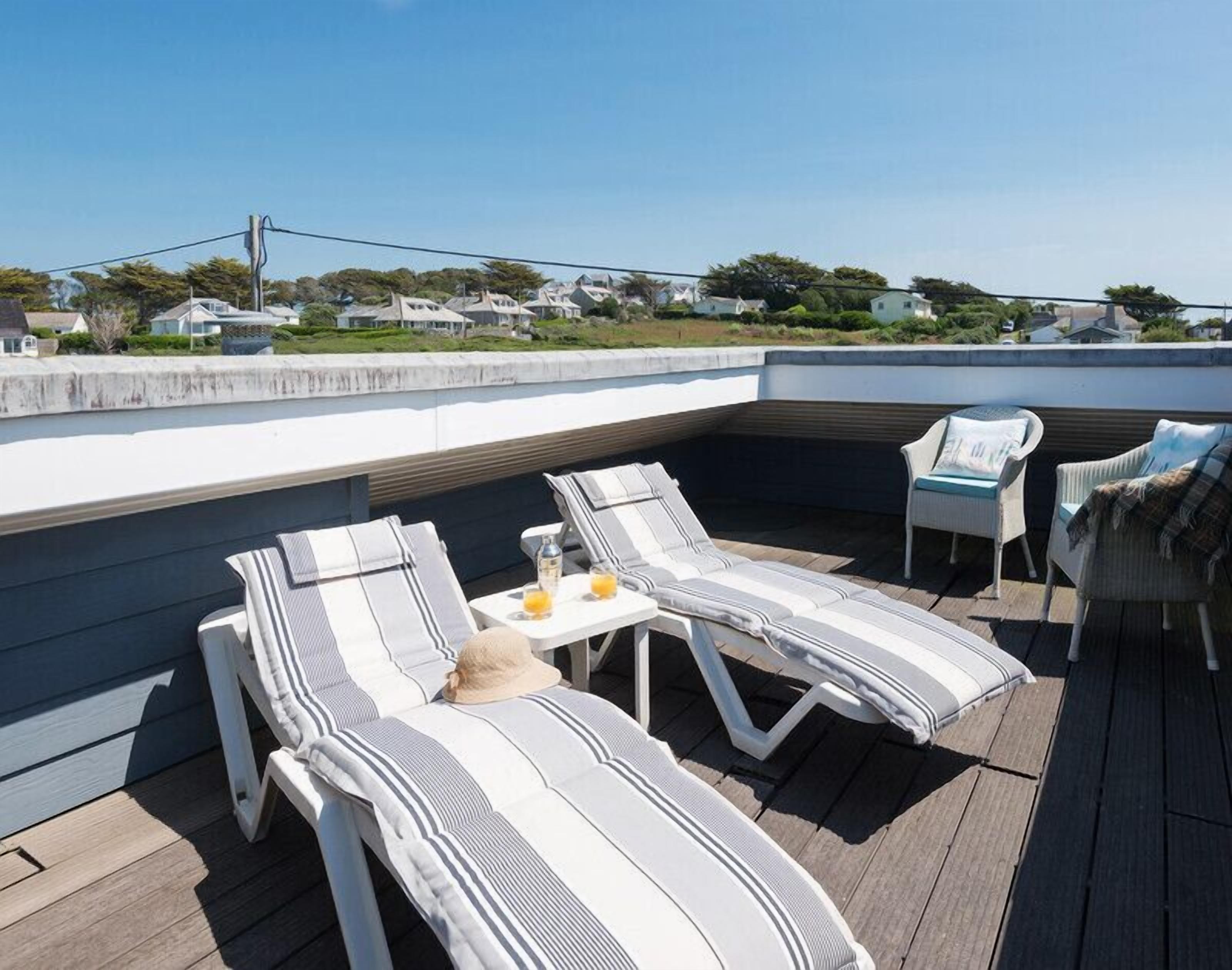 A rooftop patio with lounge chairs and a table, overlooking a residential area.