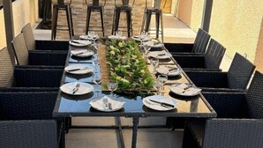 An outdoor dining area with a long table set for six, surrounded by black wicker chairs, under a pergola with hanging lights. - House 14 pers Heated pool center Valras-Plage (Valras-Plage)