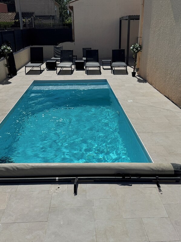 Une piscine rectangulaire à l’eau d’un bleu limpide, entourée d’une terrasse carrelée avec des chaises longues et un pot de fleurs.