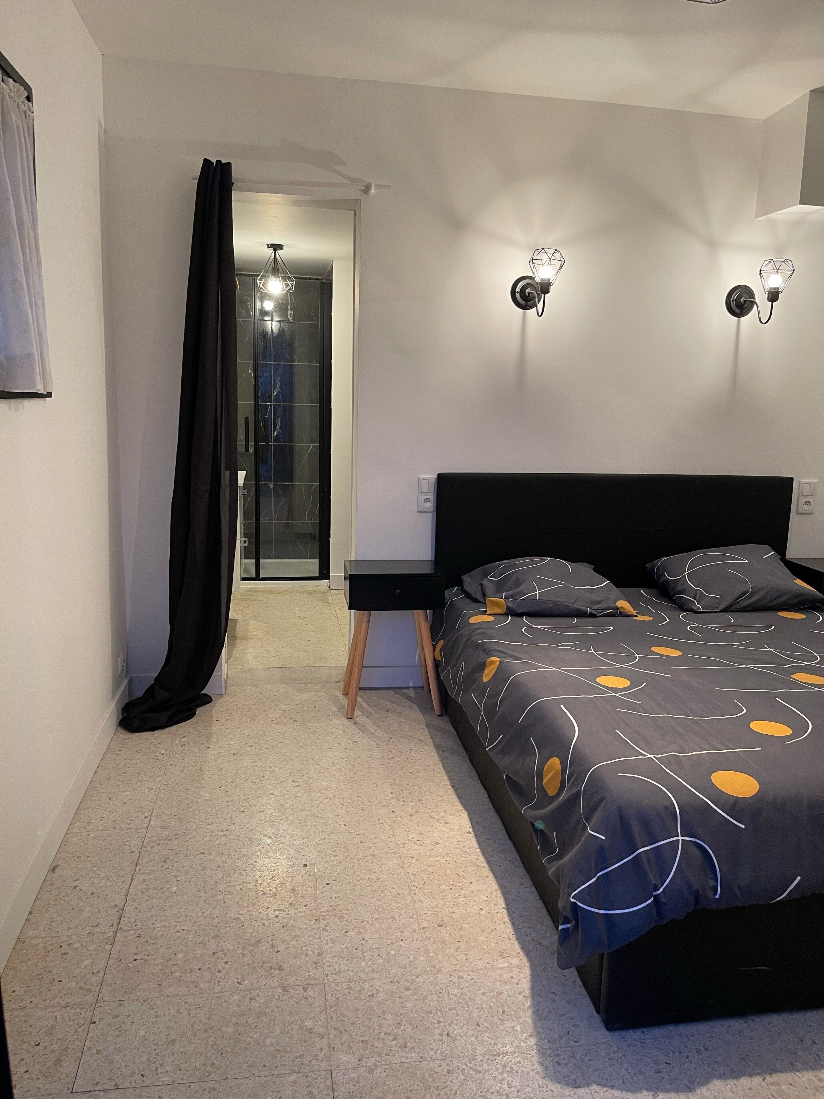 A modern bedroom with a bed, bedside tables, and a glass shower enclosure.