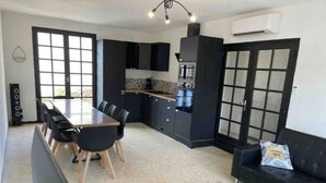 A modern kitchen with black cabinets, a dining table with chairs, a coffee machine, and a small seating area with a sofa and a side table. - House 14 pers Heated pool center Valras-Plage (Valras-Plage)